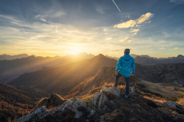 Man on stone on the hill and beautiful mountains in haze at colorful sunset in autumn. Dolomites,...