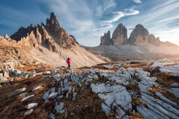 Photo sur Plexiglas Dolomites Walking girl with backpack on the trail in mountains at sunset in autumn. Tre Cime, Dolomites, Italy. Beautiful landscape with young woman, high rocks, path, stones, orange grass, sky in fall. Hiking
