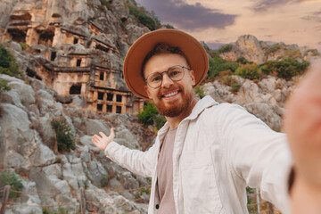 Man tourist in hat make selfie photo background old tomb Myra Ancient City in Demre to Antalya sun...