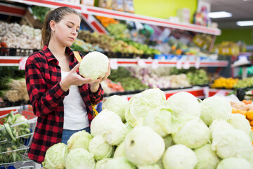 Portrait of a young female customer in a store near the counter, choosing cabbage to buy