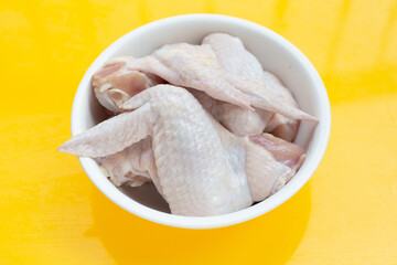 Fresh raw chicken wings in white bowl on yellow background.