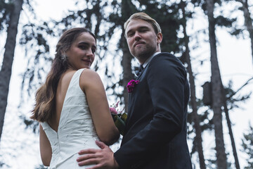 Just married forest photoshoot. Medium portrait of long-haired brunette Turkish bride and her Scandinavian husband looking back at camera with smiles on their faces. . High quality photo