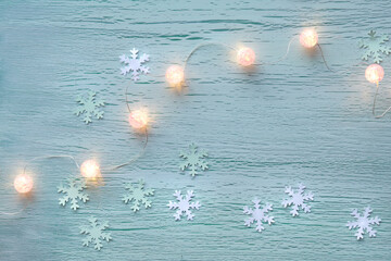 Winter pastel mint green background with paper snowflakes and string of shiny balls, electric Xmas...