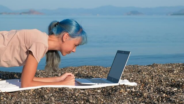 Girl online yoga against sea. A teen on the beach practice online yoga by the laptop against blue sea during summer traveling.