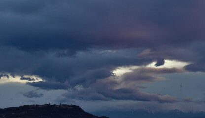 Grandi nuvole viola sopra al paese sulla collina e i monti e le valli degli Appennini