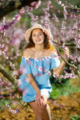 Portrait of an attractive girl in blue dress and hat in a blooming peach garden