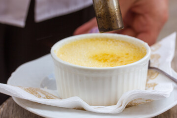 Preparing french dessert creme brulee in creme cup, torch lit with mini burner in hands of a waiter in a cafe, restaurant, pastry shop. Cooking recipe. Sweet tasty food selective soft focus close-up.