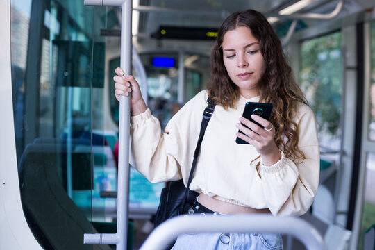 Focused girl riding in a public transport is texting with friends on a mobile phone