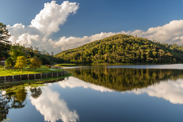 a beautiful view of a mountain with trees and a sky with clouds reflected in a lake