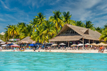 People sunbathing on the white sand beach with umbrellas, bungalow bar and cocos palms, turquoise caribbean sea, Isla Mujeres island, Caribbean Sea, Cancun, Yucatan, Mexico - obrazy, fototapety, plakaty
