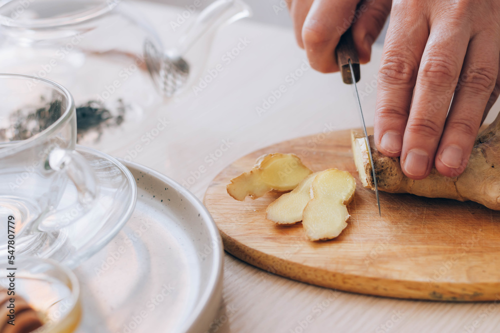 Wall mural Female hands cuts fresh ginger on table. Preparation of health tea, antioxidant drink