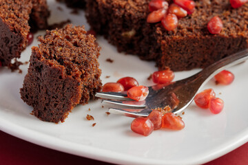 A piece of chocolate cake with pomegranate seeds served on a white plate. Close up view.