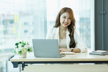 Smiling Cute asian woman working laptop happy for success. Attractive Happy female employee in the office or co-working space with copy space for label text.