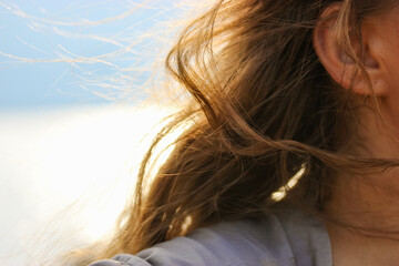 A breeze in her brown wavy curly hair selective focus. Portrait of a young woman, a girl with hair fluttering in the wind. A breezy windy day by the sea. Solo traveling, dreaming concept. Female mood.
