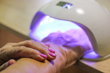Woman hand inside UV LED lamp for drying pink nails with gel method, plate curing close up....