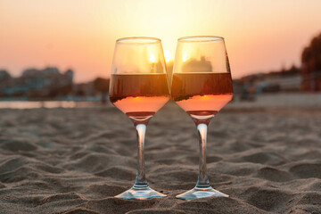 Glasses of tasty rose wine on sandy beach