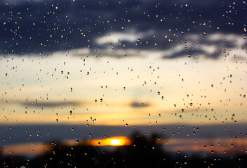 Rain at sunset. Wet window glass with raindrops against sun setting down. Autumn