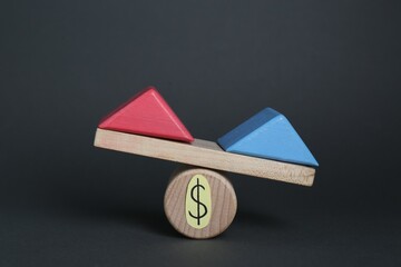 Gender pay gap. Wooden triangles as male and female symbols on miniature seesaw against black...