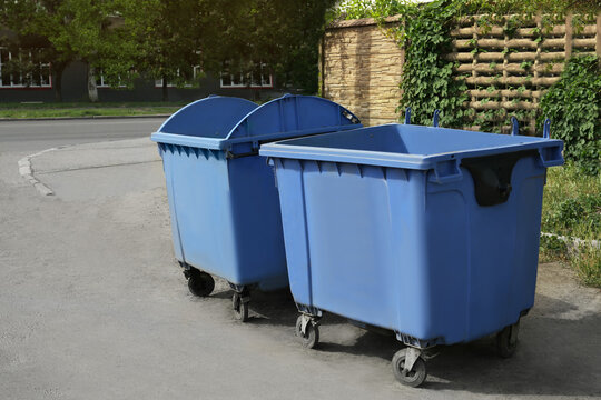 Two open blue dumpsters with wheels on city street