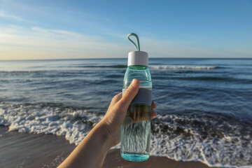 Woman holding glass bottle with water near sea, closeup