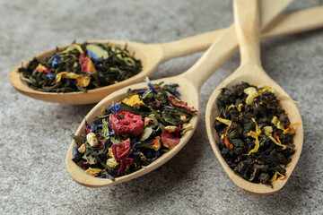 Different kinds of dry herbal tea in wooden spoons on light grey table, closeup