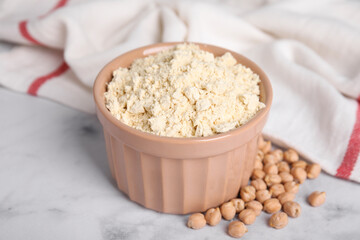 Chickpea flour in bowl and seeds on white marble table