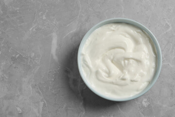 Bowl of fresh yogurt on grey table, top view. Space for text