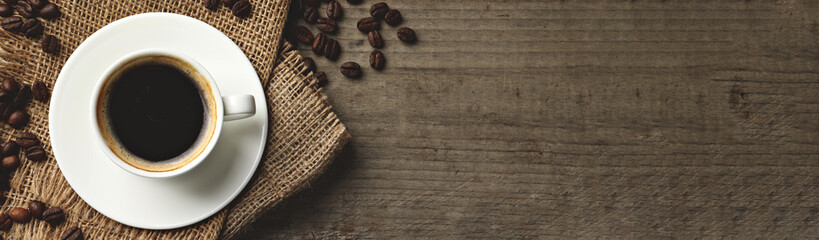 Cup of hot aromatic coffee and roasted beans on wooden table, top view with space for text. Banner...
