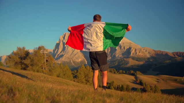 Mountains, forest and grass fields with a man holding an Italian flag filmed at Alpe di Siusi in Alps, Italian Dolomites filmed at sunset. Filmed at tight focall lenghtclose to gorund, slow motion 4k