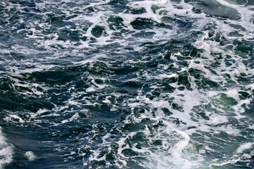 Stern waves with white foam tips on greyish blue sea water, photo taken from aboard ship. Selective...