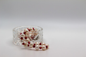 Macro abstract view of a small crystal bowl containing a Baroque pearl necklace of red and white beads, with white background