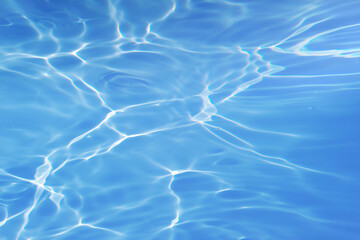 Bluewater waves on the surface ripples blurred. Defocus blurred transparent blue colored clear calm water surface texture with splash and bubbles. Water waves with shining pattern texture background.
