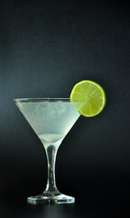 Margarita cocktail with ice and a thin slice of lime on a black background.