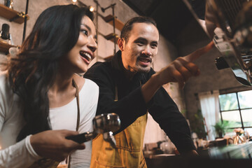 portraits of happiness two waiter teaching woman with apron to use a coffee machine for make a coffee. the happiness men and woman in bakery small business on waiter and waitress uniform.