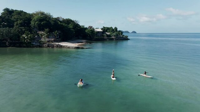 Static drone footage of three people making yoga poses on paddle board in the middle of the sea 