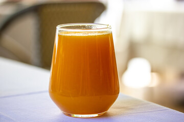 A stylish glass with orange fresh, carrot, peach juice. A refreshingly sweet drink stands on a table of cafe, restaurant terrace. Glass with non-alcoholic beverage on white tablecloth. Detox drinks.