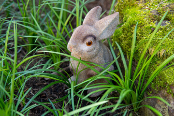 Toy brown bunny sits in the green grass, closeup. Symbol of the year 2023