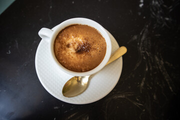 Porcelain white coffee cup with cappuccino, mochaccino on a saucer with a teaspoon on a black...