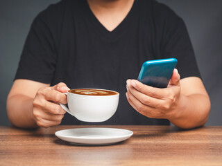 Hands of a man holding a smartphone and coffee cup while sitting at the table