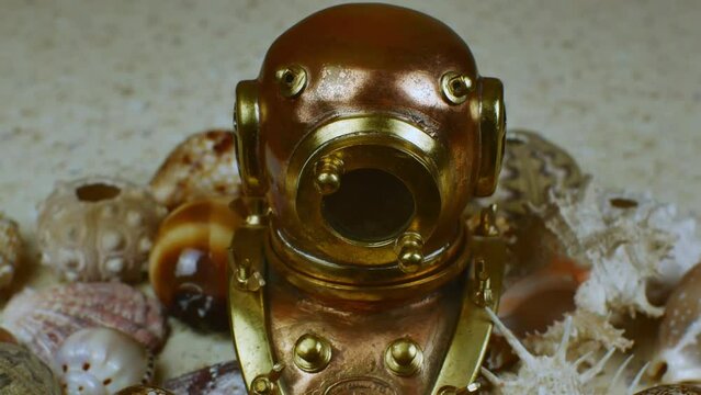 Miniature copper retro diving helmet surrounded by various beautiful sea shells. The concept of the history of diving equipment