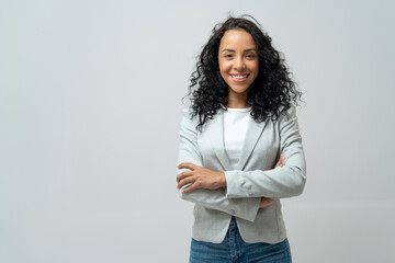 Portrait of smiling latin woman with curly hair with crossed arms isolated on grey background.