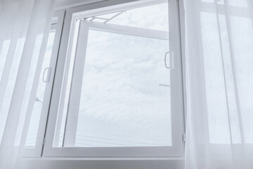 Window frame with soft curtains. Open to the wind blow of summer breeze. Bright sky daylight and fresh air from outside.