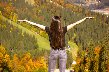 Beautiful slender slim girl, young woman with long brown hair stands on mountain top with raised...