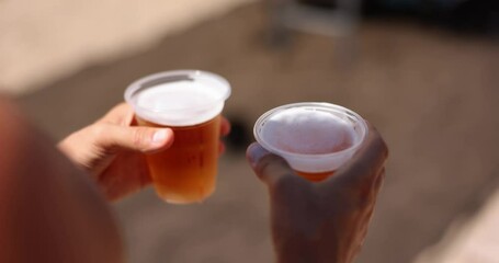 Persons hand holding two glasses of refreshing beer on beach - Powered by Adobe