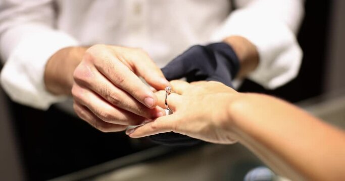 Jeweler in gloves puts beautiful diamond engagement ring on woman finger