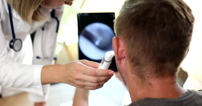 ENT doctor looks into patient ear using digital otoscope with image on screen