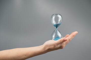 Woman holding an hourglass on a gray background. Close-up. Copy space. 