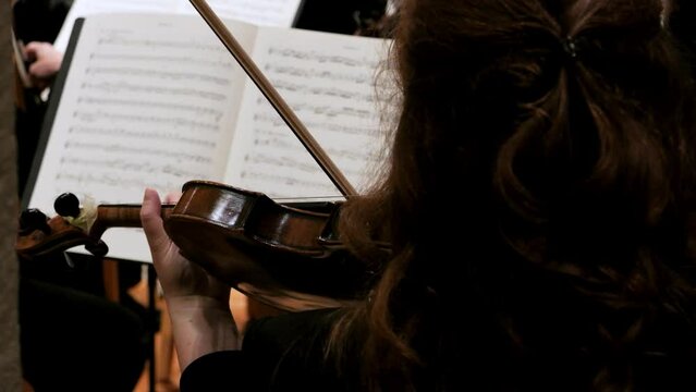 Extreme close up shot of a talented violin player with wooden violin during a concert to classical music looking at her music stand with sheet music. Slow Motion