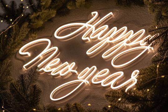 Christmas Decor. A Flexible Neon Sign With The Words Happy New Year Hanging On The Wall. Around The Wreath Of Christmas Tree Branches. Celebration Of New Year, Christmas