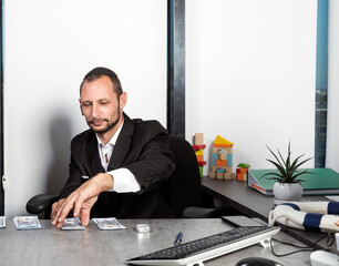 Serious jewish man in formal wear sit at desk wearing kippah with surprised looking at dollar bills. Caucasian man is putting hundred dollar bills on the table as payment. Jew receiving salary money - obrazy, fototapety, plakaty